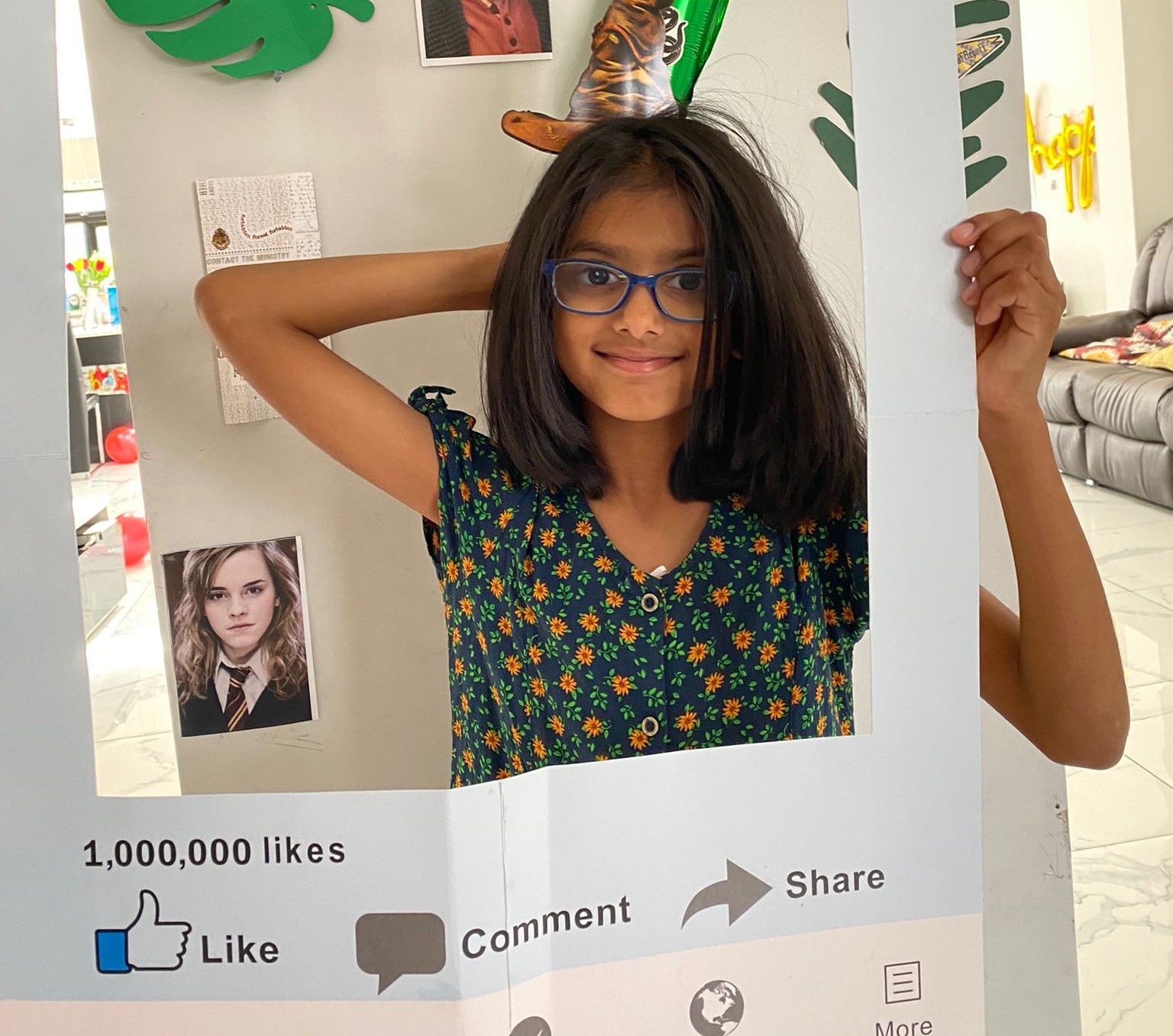 Donate cropped image Riya wears a floral dress and smiles in front of a cardboard frame that she holds with her left hand.