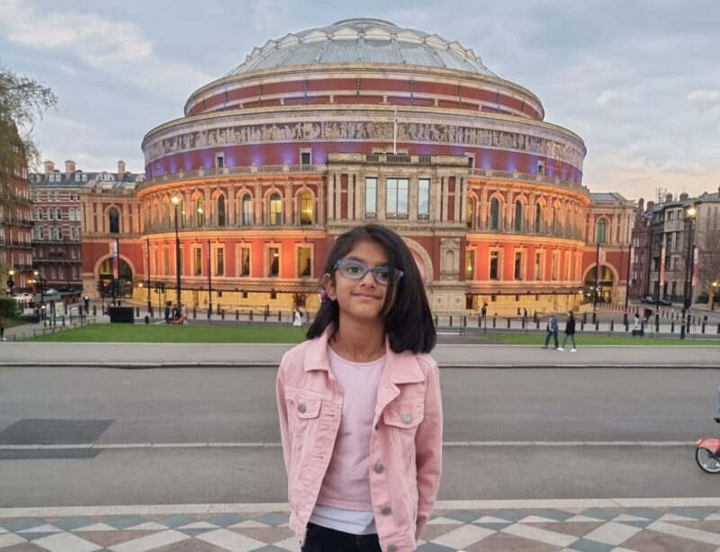Sisters Riya wearing a pink denim jacket, smiles in front of
